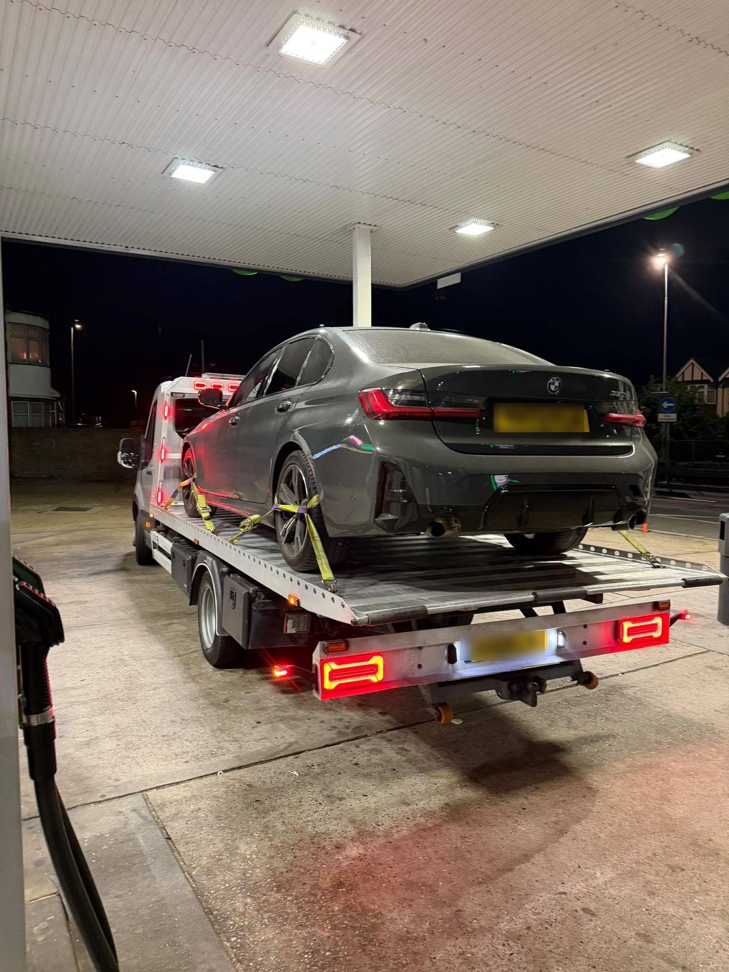 Emergency vehicle recovery of a grey BMW at a petrol station at night