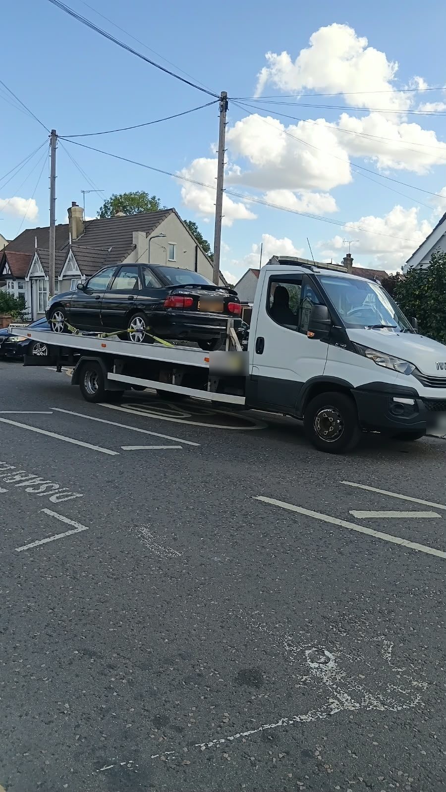 Recovery truck carrying a dark saloon on a suburban road