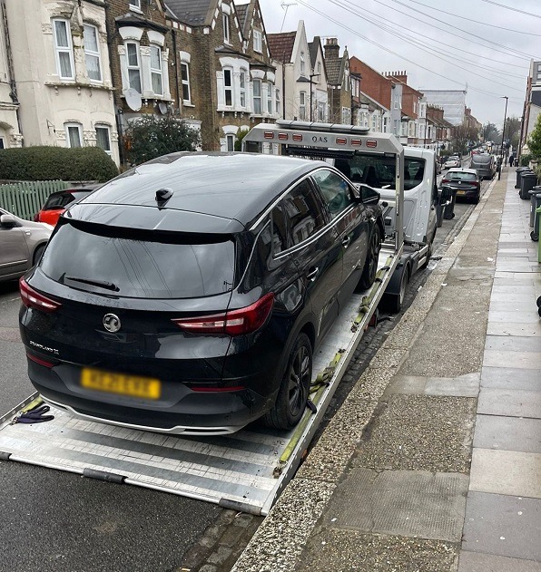 Black Vauxhall SUV loaded on a recovery truck on an East London street