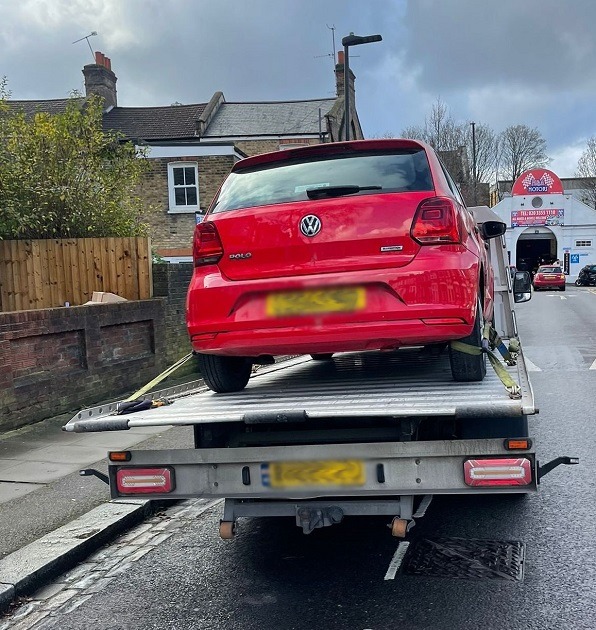 Red VW Polo strapped onto a flatbed recovery truck in a residential street