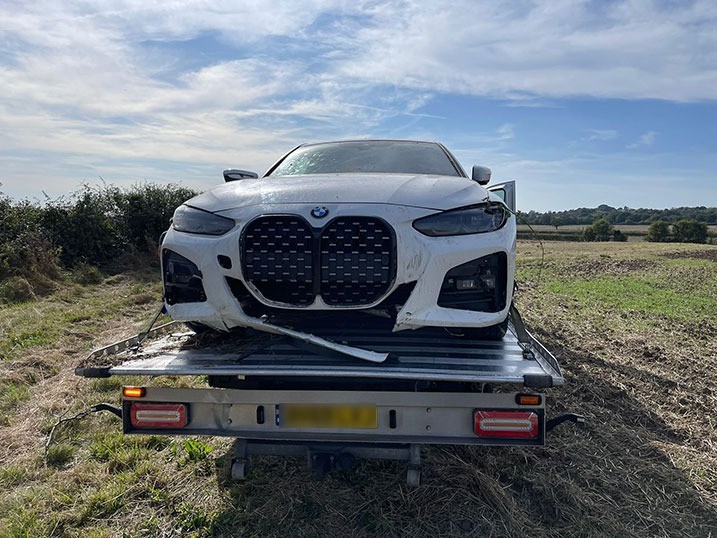 Damaged white BMW loaded onto a recovery truck in a field