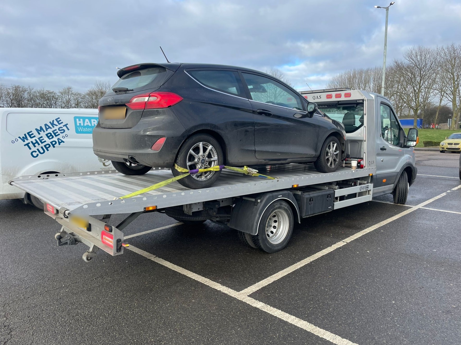 Grey Ford Fiesta strapped onto a recovery truck in a car park