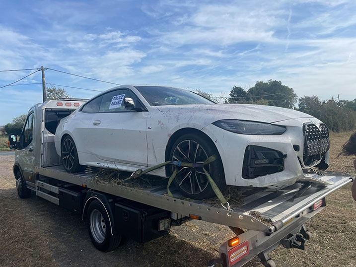 White BMW coupe secured on a flatbed truck in the countryside