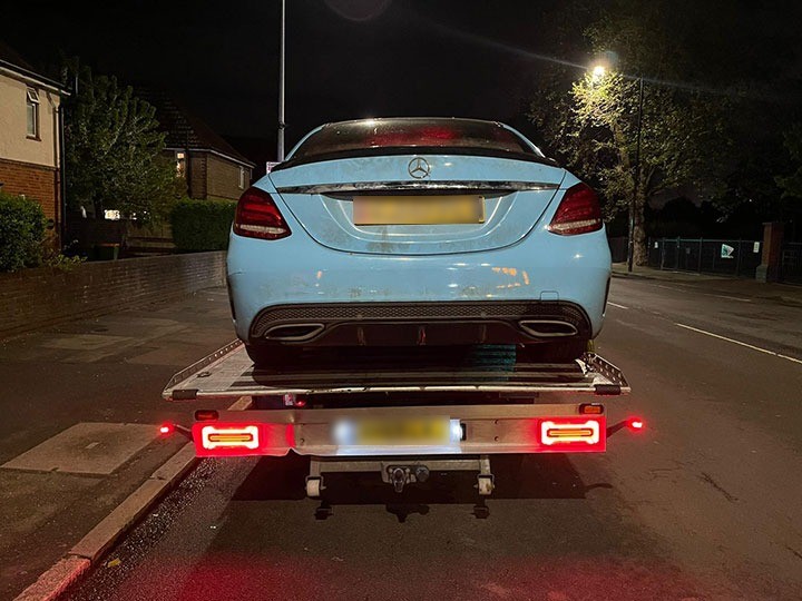 Mercedes saloon on a recovery truck at night with lights on