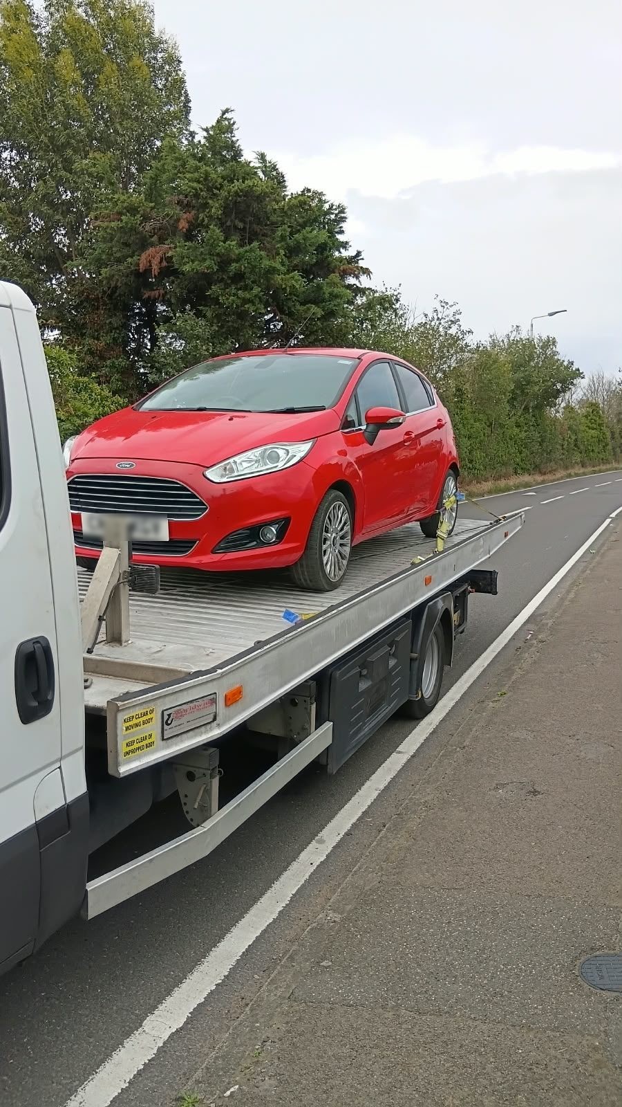 Red Ford Fiesta strapped onto a flatbed towing truck at the roadside