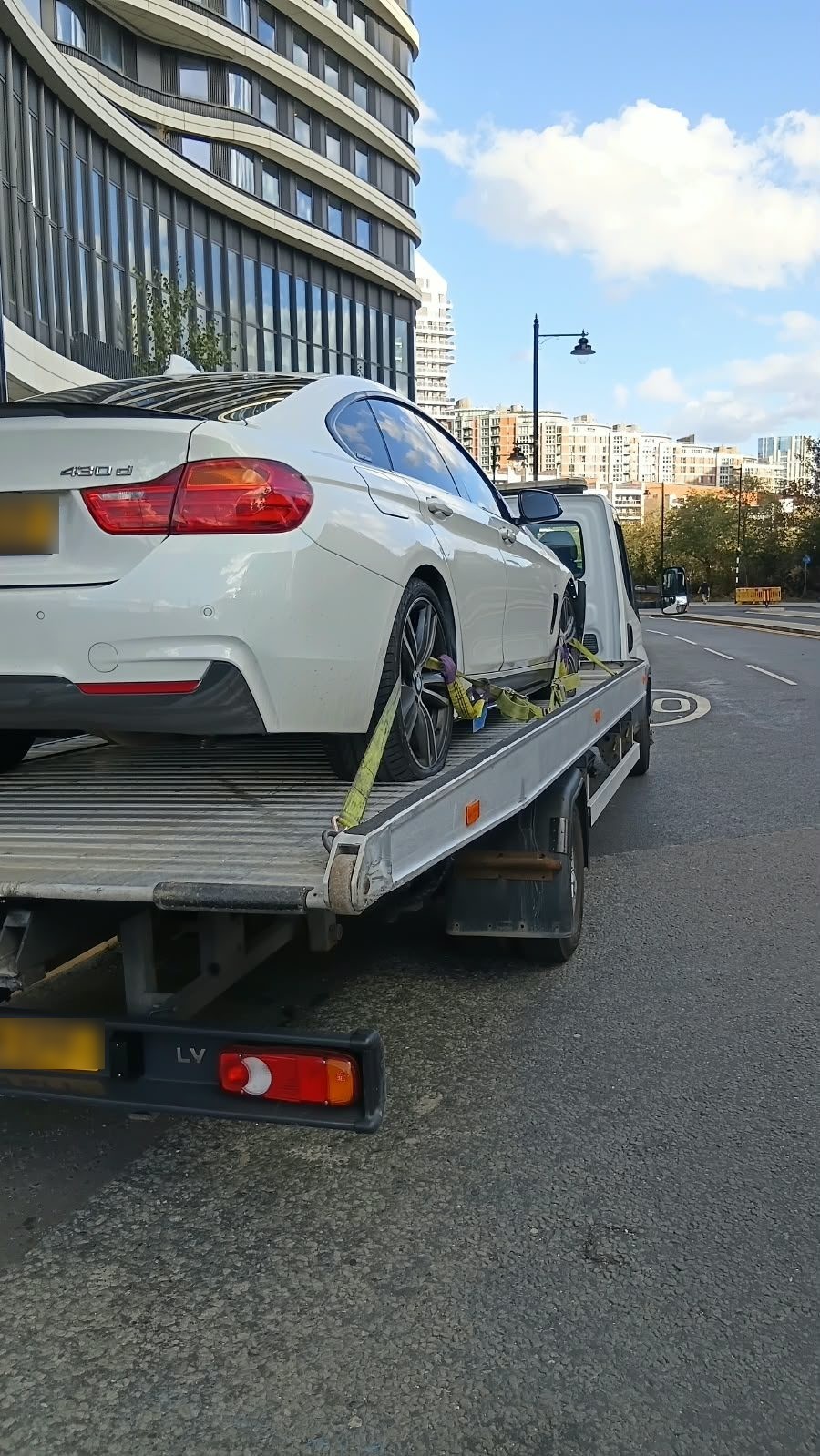 Recovery truck carrying a white BMW past city flats